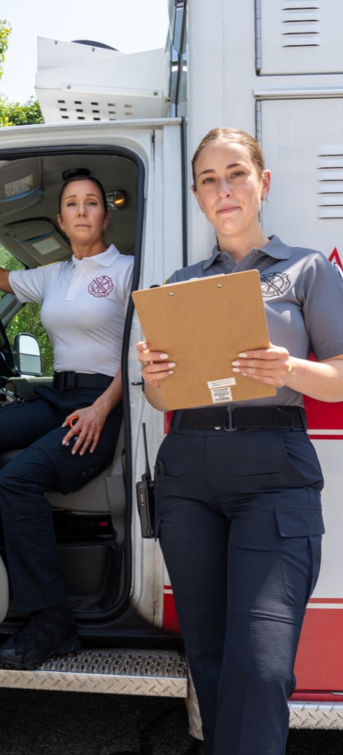 Two female EMTs wear women's performance polos in an ambulance