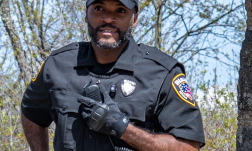 An officer wears a Navy Vest Carrier, matching short sleeve Navy Base Shirt, and hat and gloves for a cohesive, matching uniform look