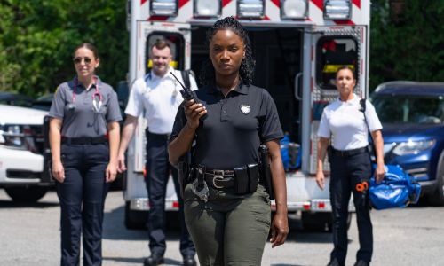 Female officer leads a team of responders in front of an ambulance and police car